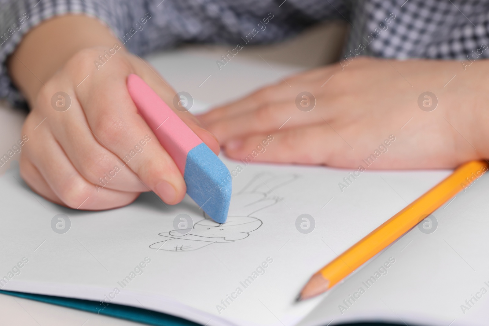 Photo of Boy erasing mistake in his notebook at white desk, closeup