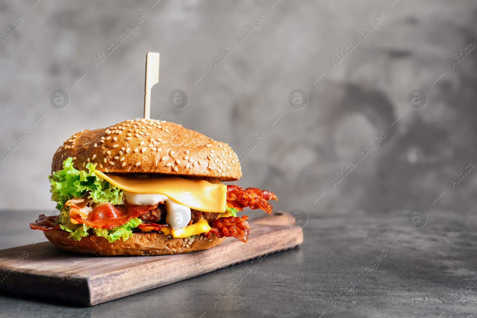 Photo of Tasty burger with bacon on wooden board