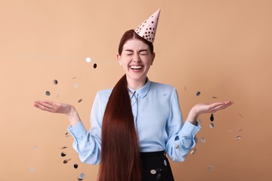 Photo of Happy woman in party hat and falling confetti on beige background