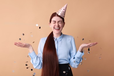 Happy woman in party hat and falling confetti on beige background