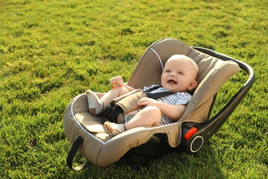 Adorable baby in child safety seat on green grass