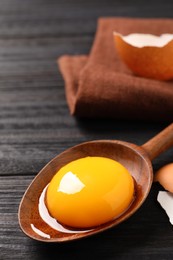 Photo of Spoon with raw egg yolk on black wooden table, closeup