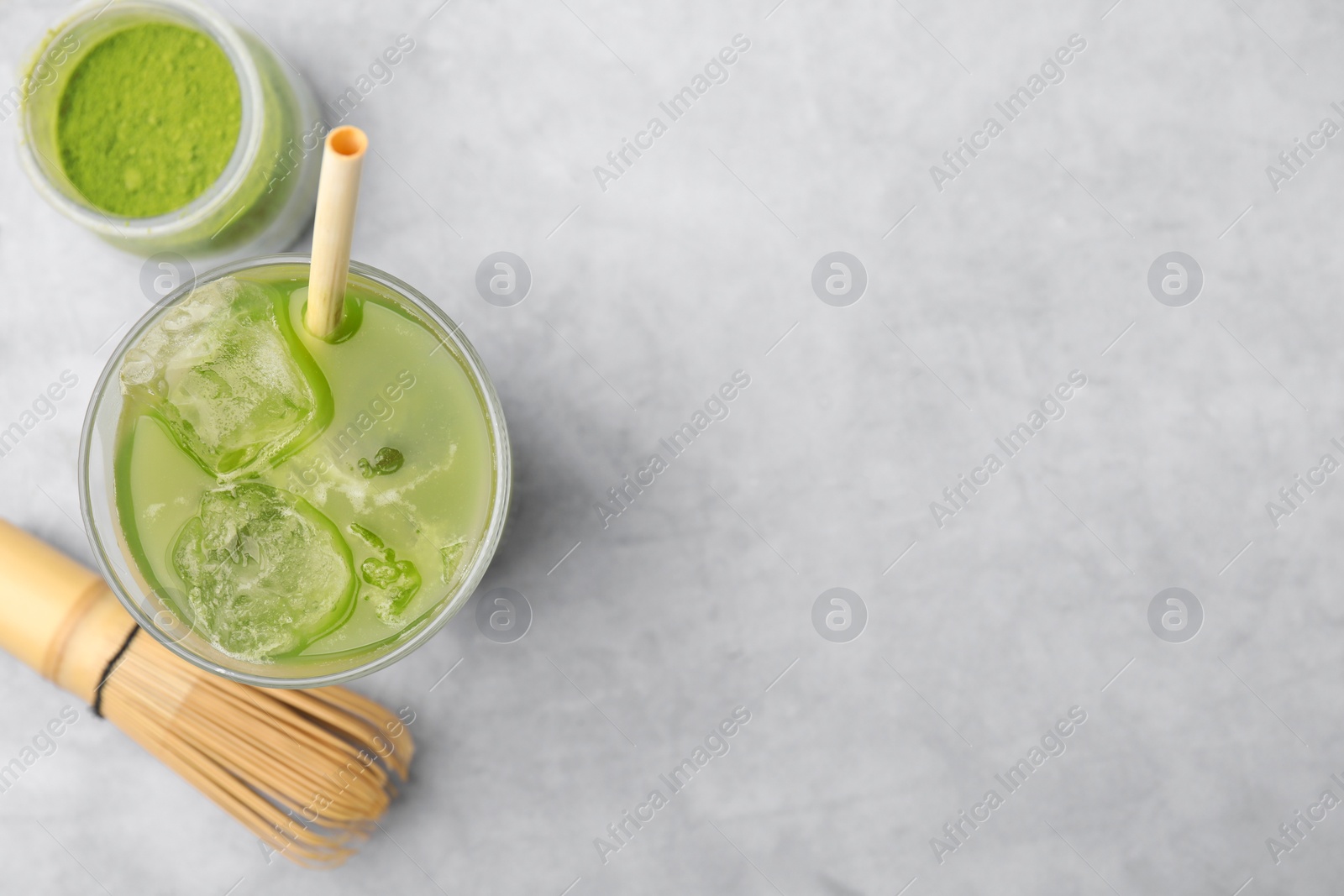 Photo of Glass of delicious iced green matcha tea, powder and bamboo whisk on light grey table, flat lay. Space for text