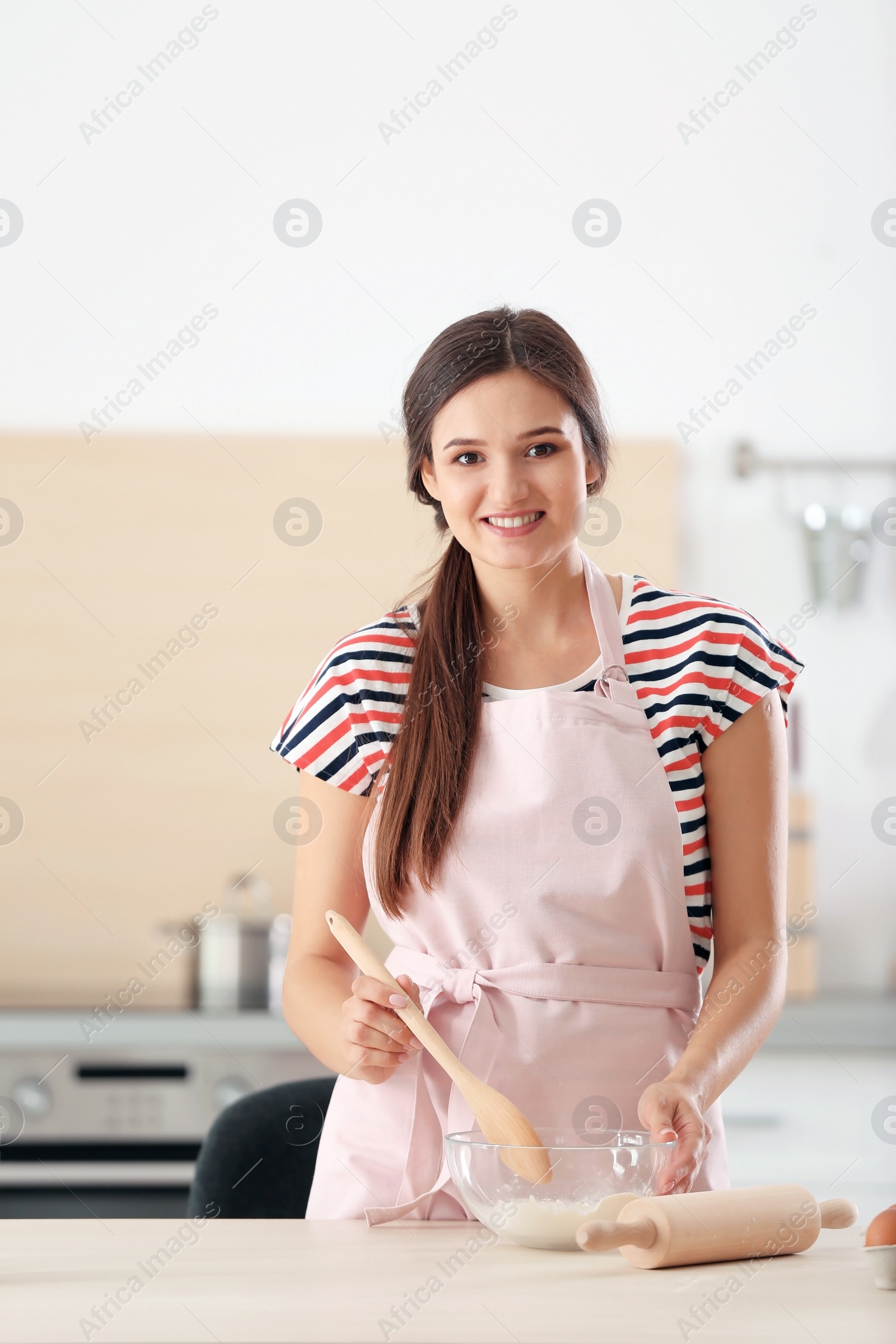 Photo of Young woman making dough at table in kitchen