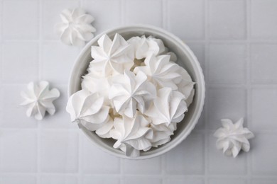 Delicious meringue cookies in bowl on white tiled table, flat lay