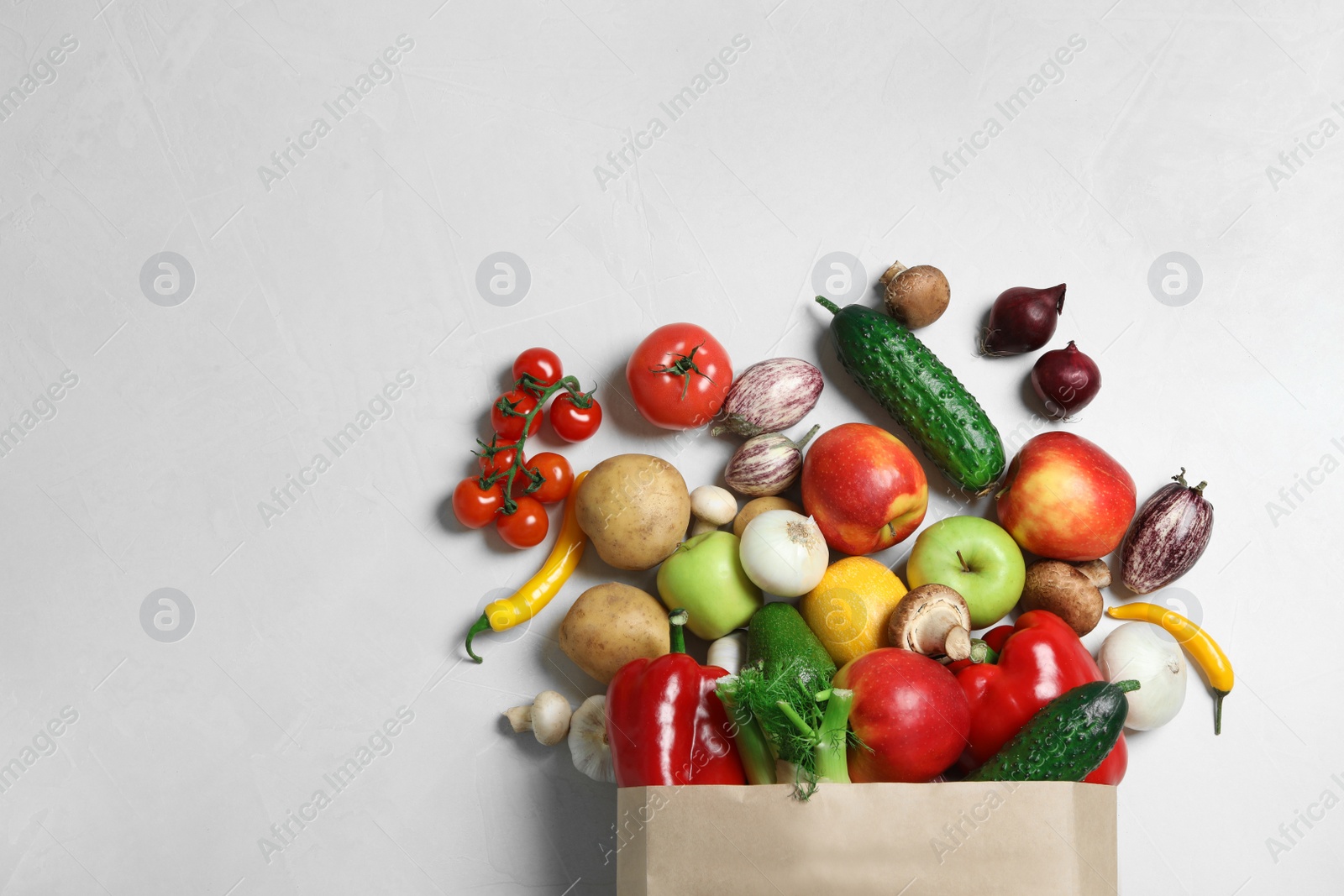 Photo of Paper bag with fresh vegetables and fruits on light background, flat lay. Space for text