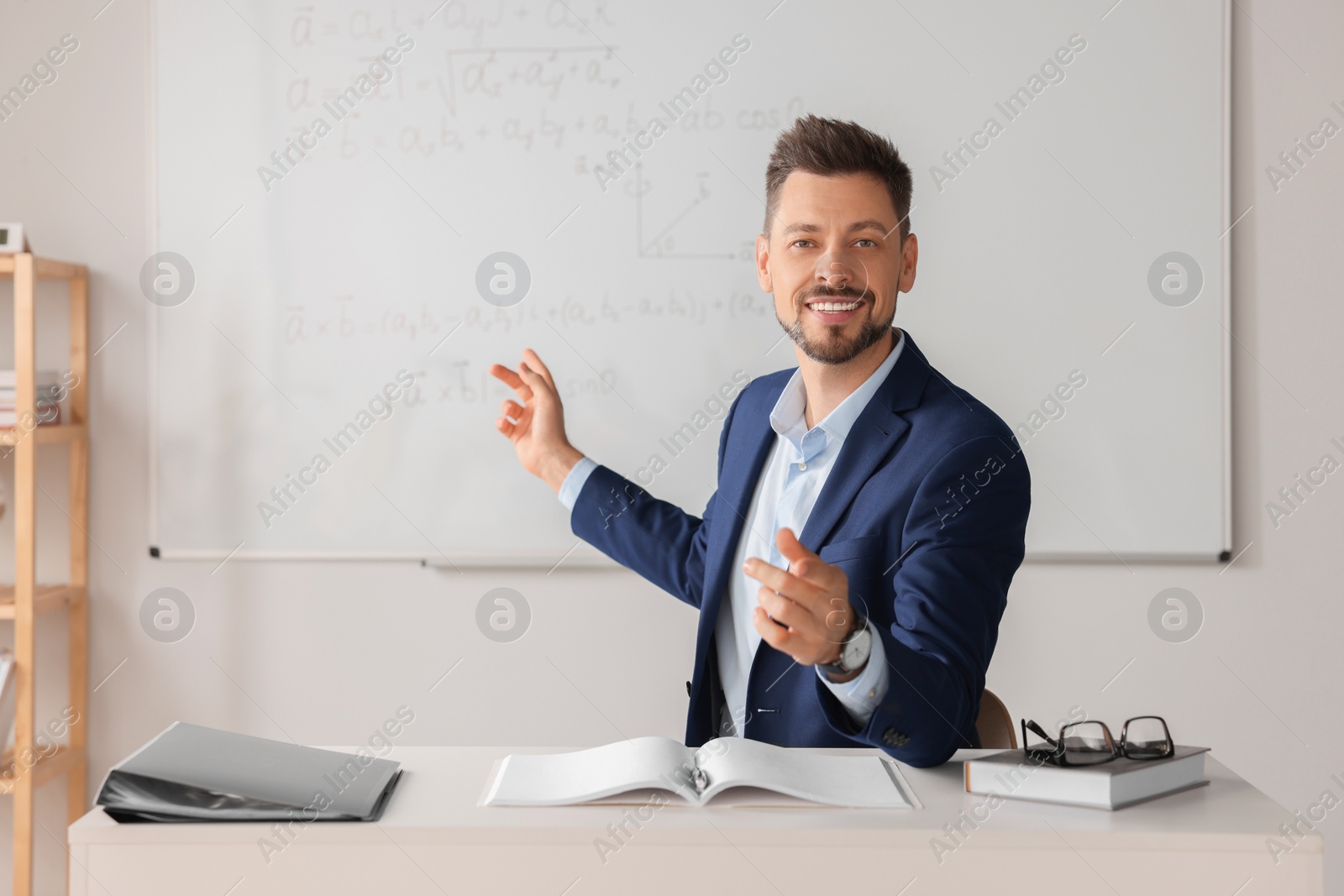 Photo of Happy teacher explaining mathematics at table in classroom