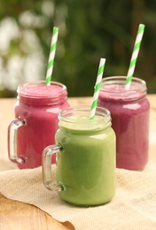 Different delicious smoothies in mason jars on wooden table against blurred background