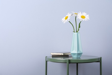 Photo of Beautiful tender chamomile flowers in vase and notebooks on table against light background, space for text