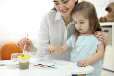 Photo of Mother and her little daughter painting with watercolor at home, closeup