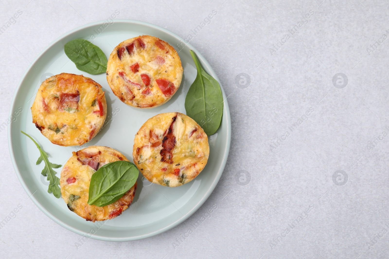 Photo of Freshly baked bacon and egg muffins with cheese on light gray table, top view. Space for text