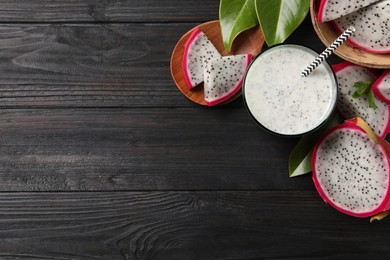 Photo of Delicious pitahaya smoothie and fresh fruits on black wooden table, flat lay. Space for text