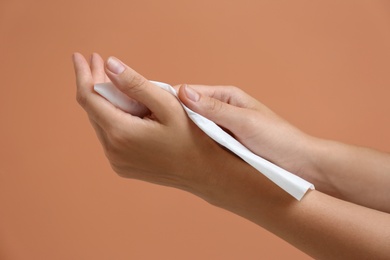 Photo of Woman cleaning hands with paper tissue on light brown background, closeup