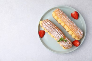 Photo of Delicious eclairs filled with cream, strawberries and mint on light table, top view. Space for text