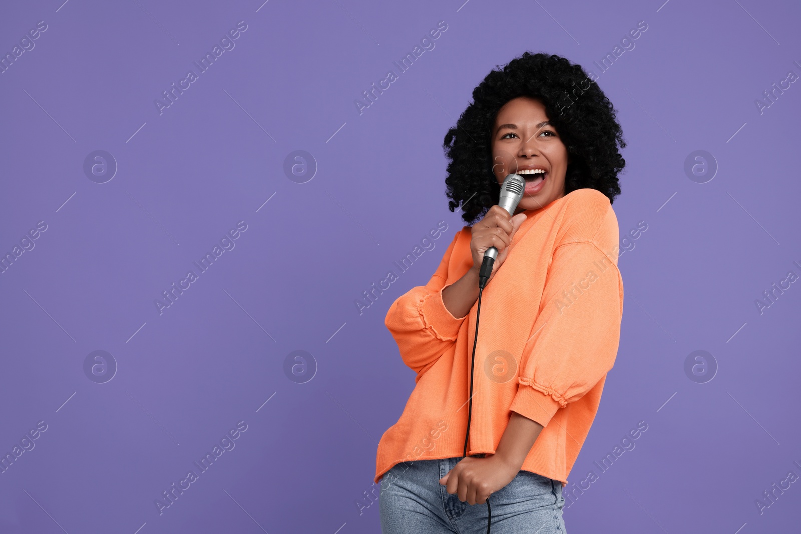 Photo of Beautiful woman with microphone singing on violet background, space for text