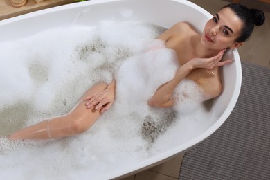 Woman taking bath with shower gel indoors, above view