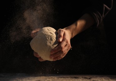 Photo of Making bread. Woman kneading dough at table on dark background, closeup