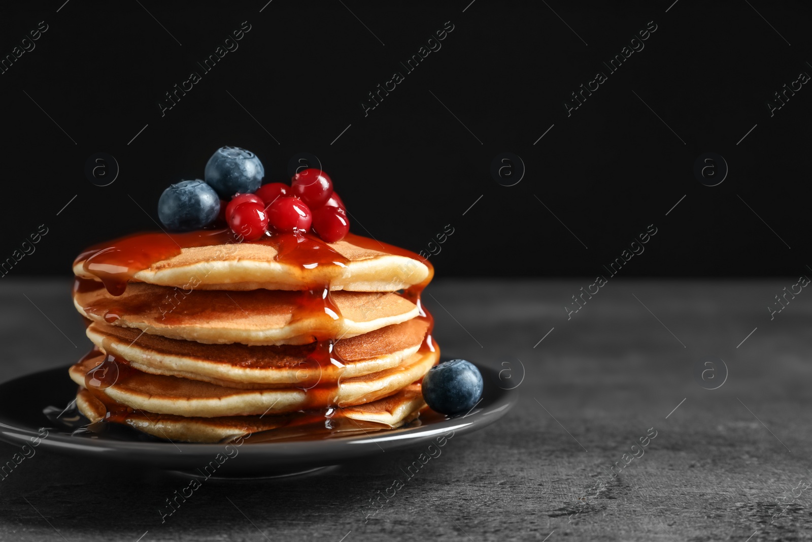 Photo of Stack of tasty pancakes with berries and syrup on table