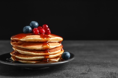 Stack of tasty pancakes with berries and syrup on table