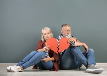 Photo of Mature couple with torn paper heart indoors. Relationship problems