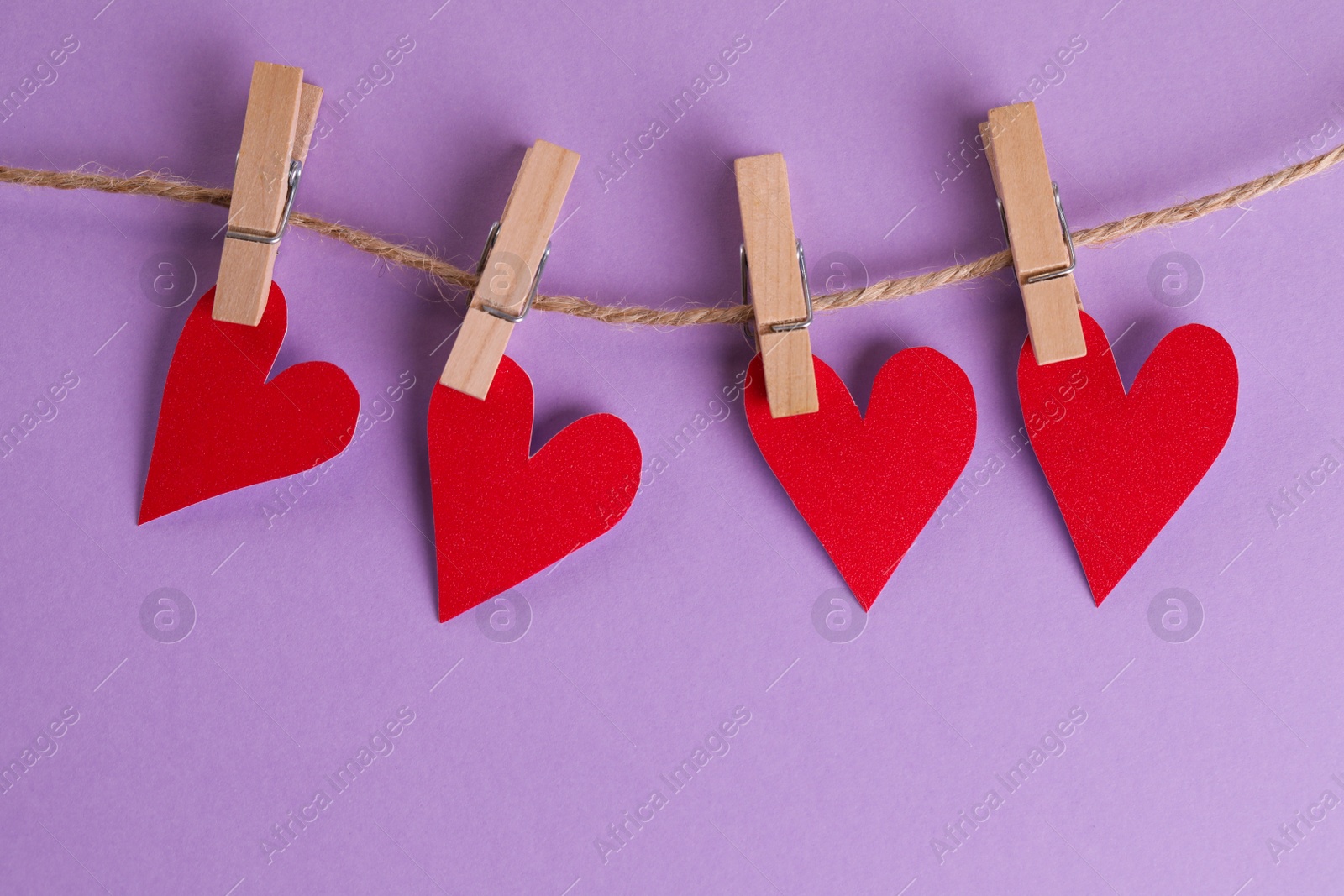 Photo of Red hearts and rope with clothespins on violet background, top view. St. Valentine's day