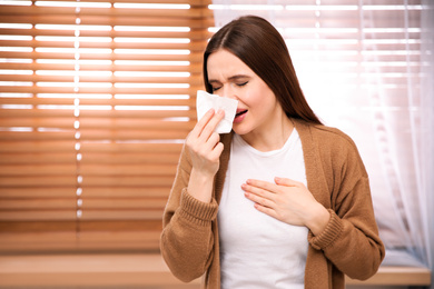 Photo of Sick young woman sneezing at home. Influenza virus