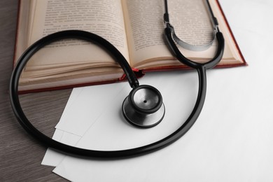 Book, stethoscope and sheets of paper on wooden table. Medical education