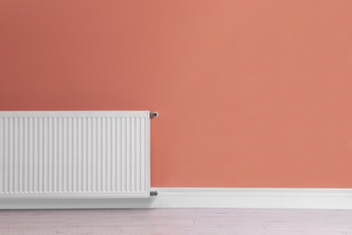 Photo of Modern radiator on color wall, space for text. Central heating system