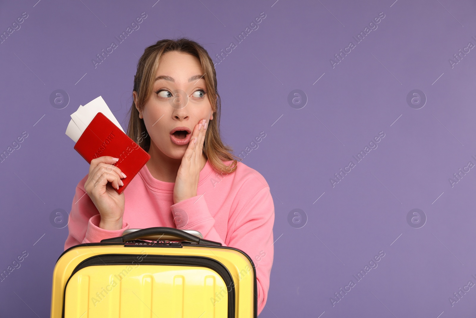 Photo of Happy young woman with passport, ticket and suitcase on purple background, space for text