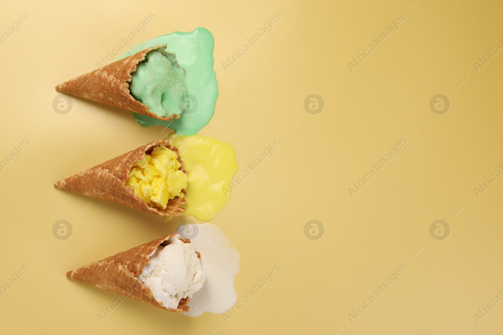 Photo of Melted ice cream in wafer cones on pale yellow background, flat lay. Space for text