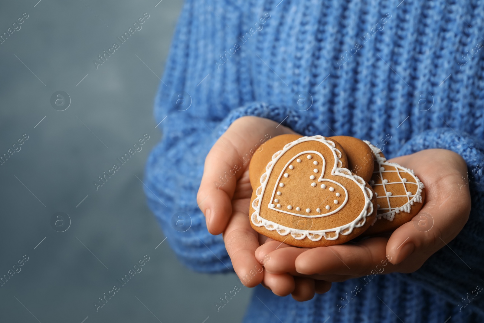 Photo of Woman with tasty heart shaped gingerbread cookies on blue background, closeup