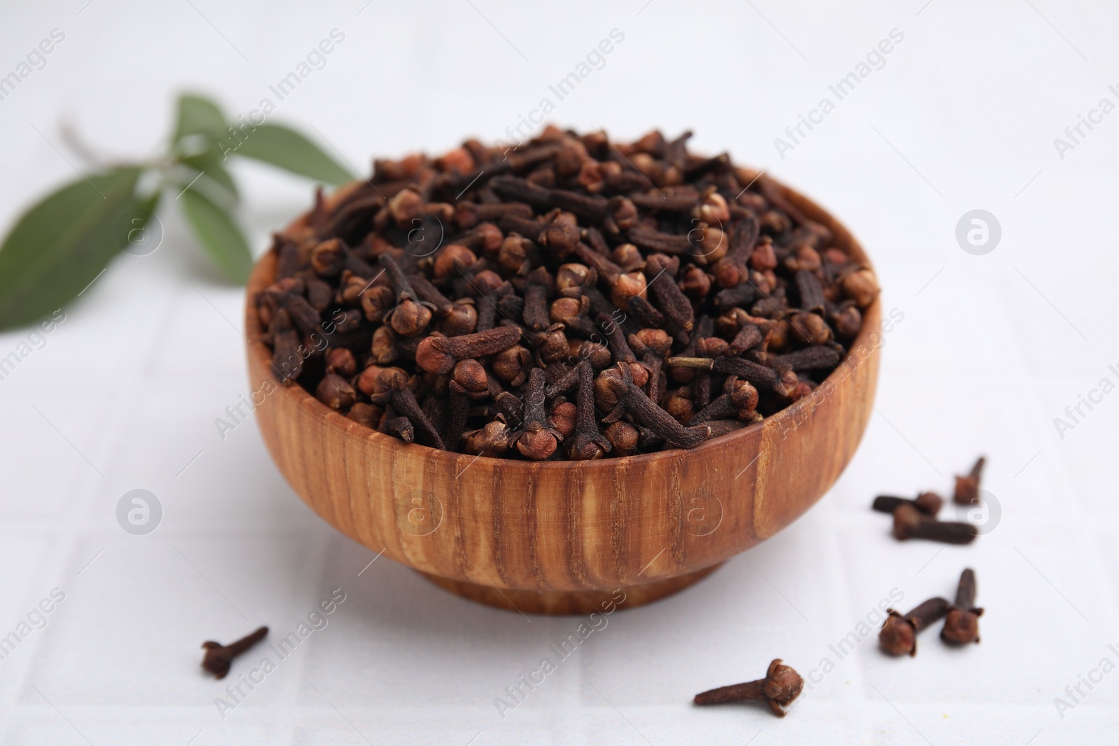 Photo of Aromatic cloves in bowl on white tiled table, closeup