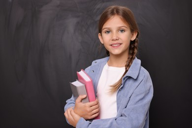 Photo of Portrait of smiling schoolgirl with books near blackboard. Space for text