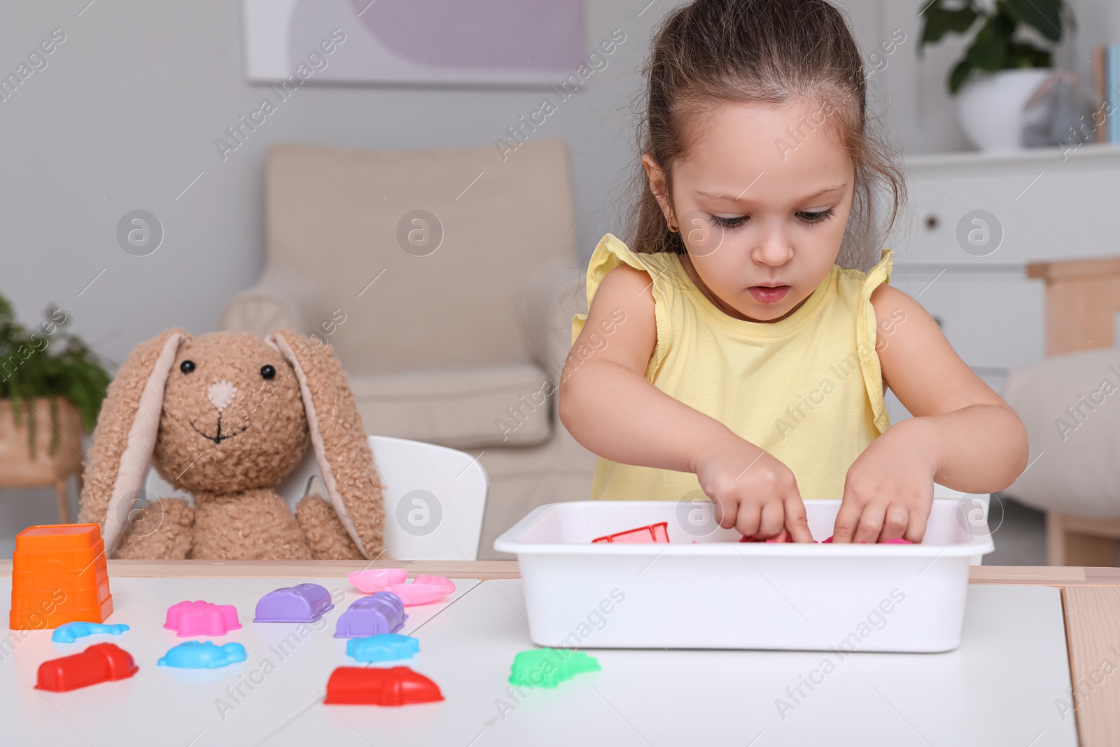 Photo of Cute little girl playing with bright kinetic sand at table in room