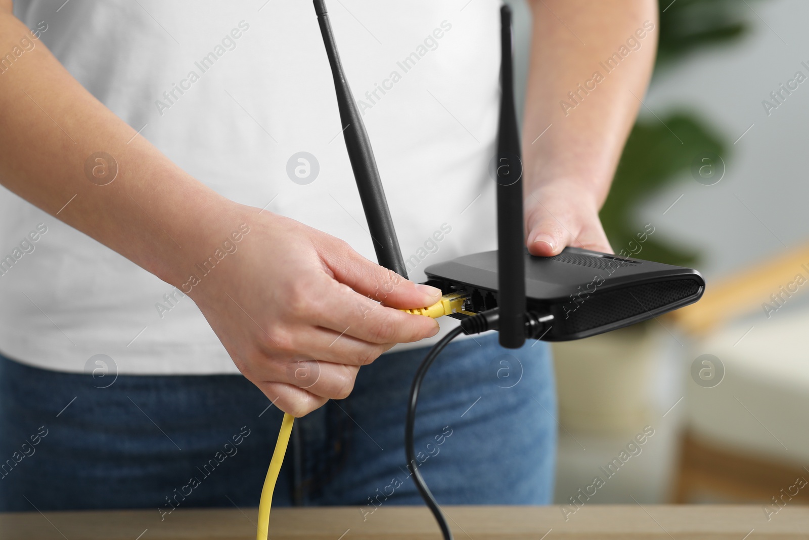 Photo of Woman inserting ethernet cable into Wi-Fi router at table indoors, closeup