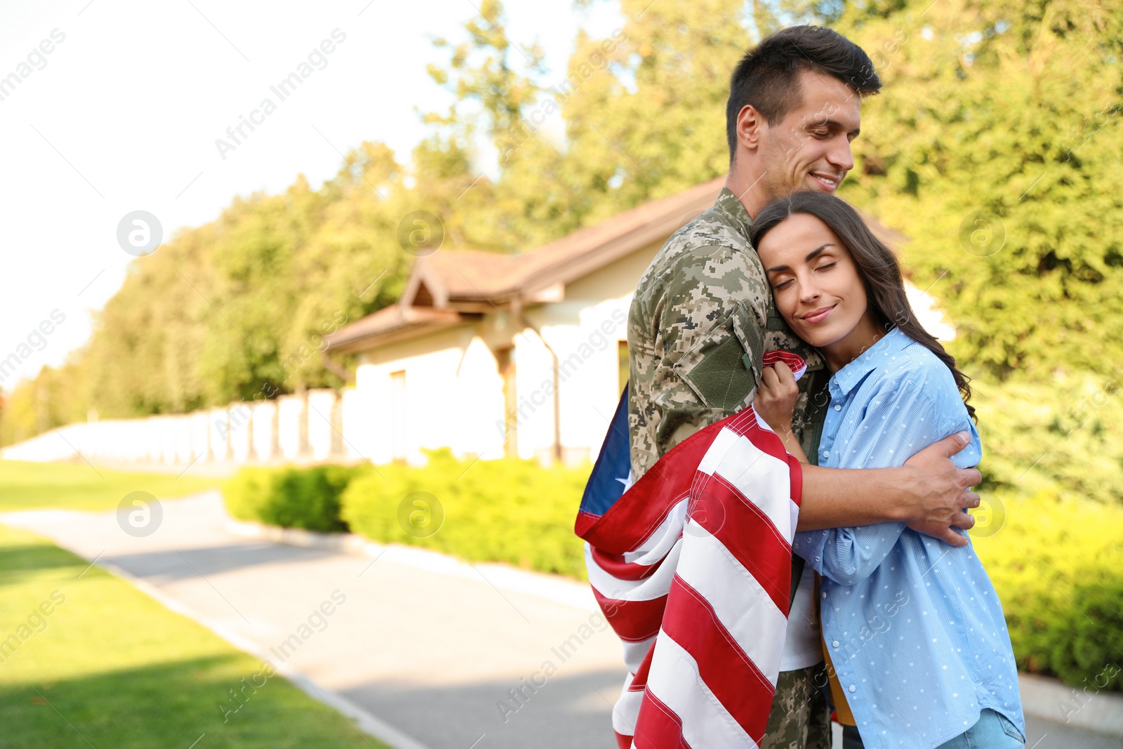 Photo of Man in military uniform with American flag hugging his wife outdoors