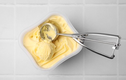 Photo of Vanilla ice cream and scoop in container on white tiled table, top view