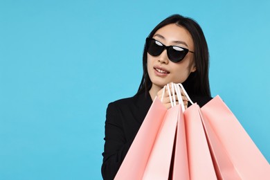 Smiling woman with shopping bags on light blue background. Space for text