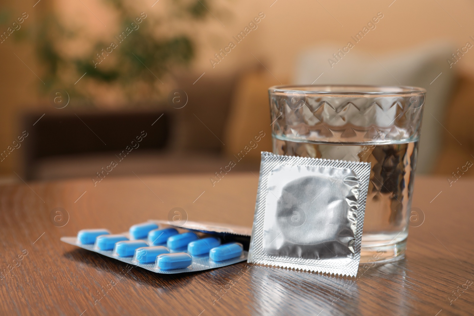 Photo of Glass of water, condoms and pills on wooden table indoors, space for text. Potency problem concept