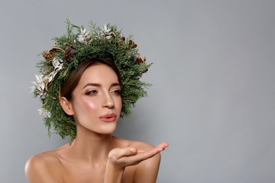 Photo of Beautiful young woman with Christmas wreath blowing kiss on grey background. Space for text
