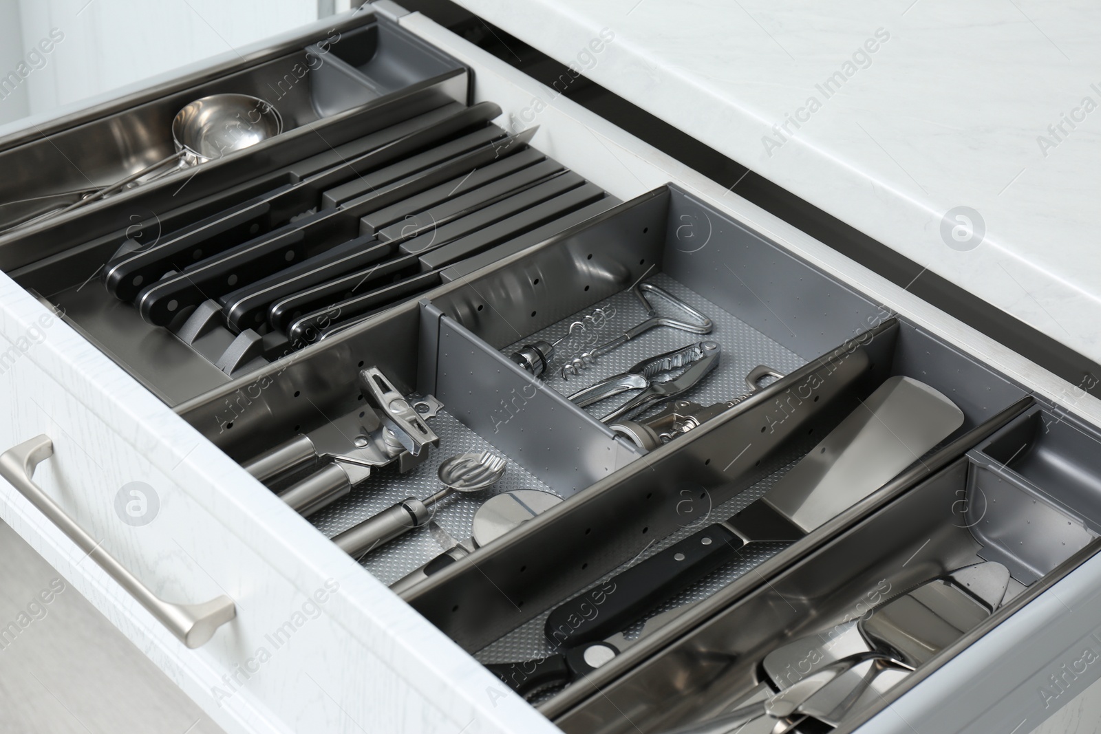 Photo of Open drawer with stainless steel utensil set, closeup. Order in kitchen