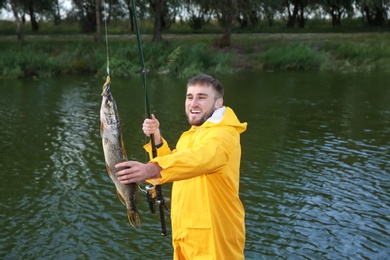 Photo of Man with rod and catch fishing at riverside. Recreational activity