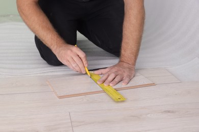 Photo of Man using measuring tape during installationlaminate flooring, closeup