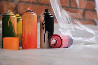 Photo of Used cans of spray paints on floor indoors. Graffiti supplies