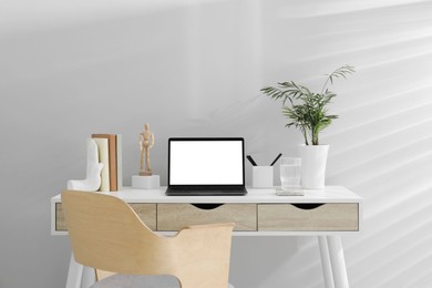 Photo of Stylish workplace with laptop, houseplant and stationery on wooden table near white wall