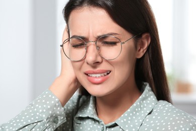 Photo of Young woman in eyeglasses suffering from ear pain indoors, closeup