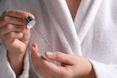 Photo of Woman applying cosmetic serum onto finger, closeup view