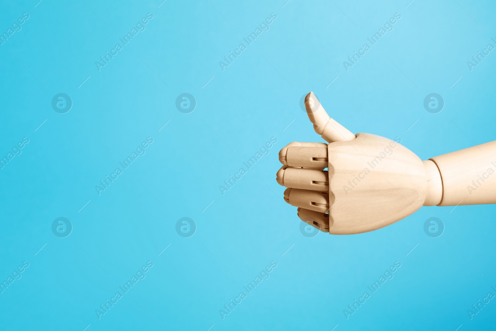 Photo of Wooden mannequin hand showing thumb up on light blue background. Space for text