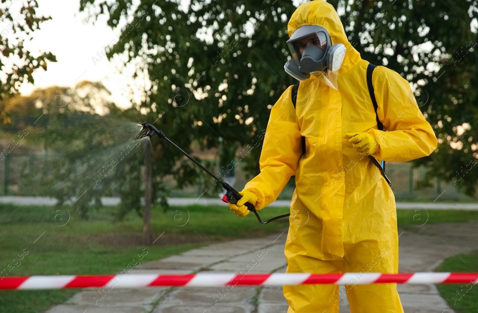 Photo of Person in hazmat suit disinfecting street with sprayer. Surface treatment during coronavirus pandemic