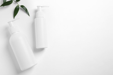 Photo of Bottles with different cosmetic products and green leaves on white background, flat lay. Space for text